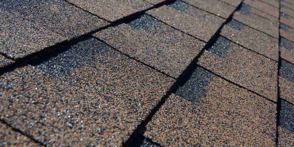 Damaged shingles are visible nearby under a blue sky.