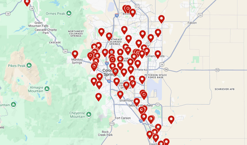 Digital map graphic of Colorado Springs terrain, densely covered with dozens of bright red location pins clustered over the city highways.