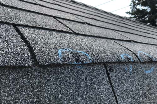 Close-up view of gray asphalt roof shingles with blue chalk circles marking areas of damage.