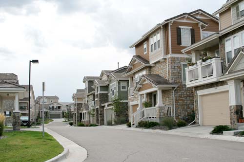 A suburban street lined with modern, multi-story townhouses under a cloudy sky.