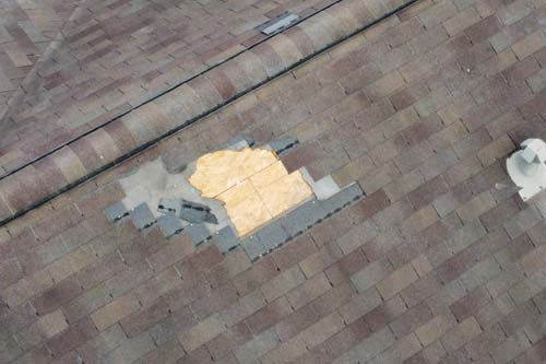 High-angle view of a damaged shingle roof with a section of missing shingles exposing the plywood deck underneath.