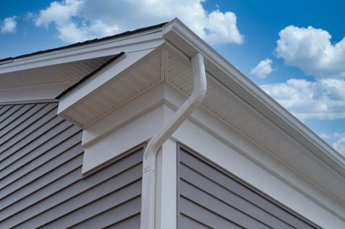White aluminum downspout and seamless gutters on a house corner with gray siding.