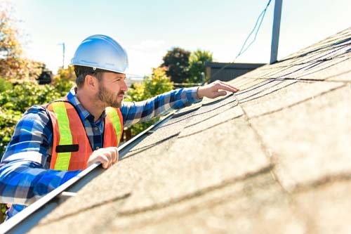 Roofing contractor inspecting a residential roof on a sunny day.