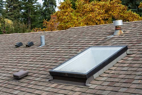 A residential shingled roof featuring a large glass skylight and multiple ventilation caps.