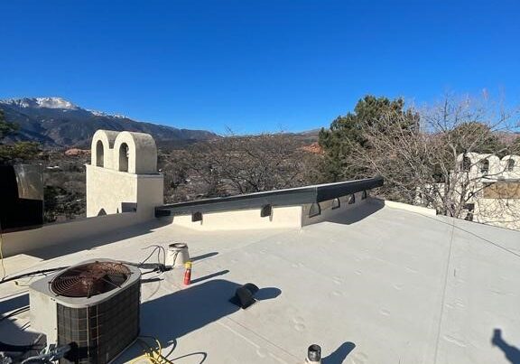 A flat, white commercial-style rooftop featuring an air conditioning condenser unit, a yellow extension cord, and small vents.