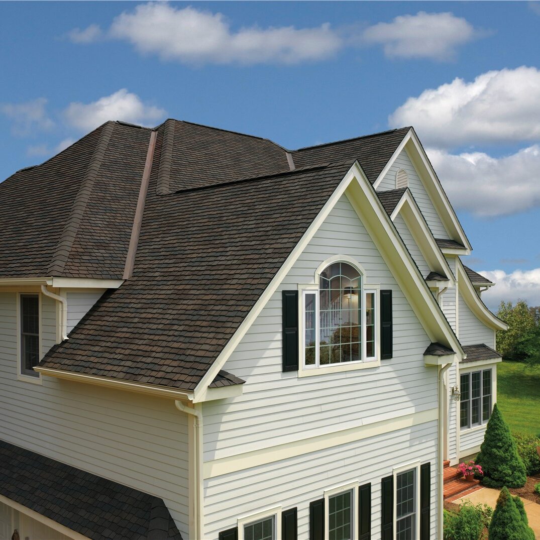 A high-angle view of a multi-gabled residential home featuring dark brown architectural asphalt shingles.
