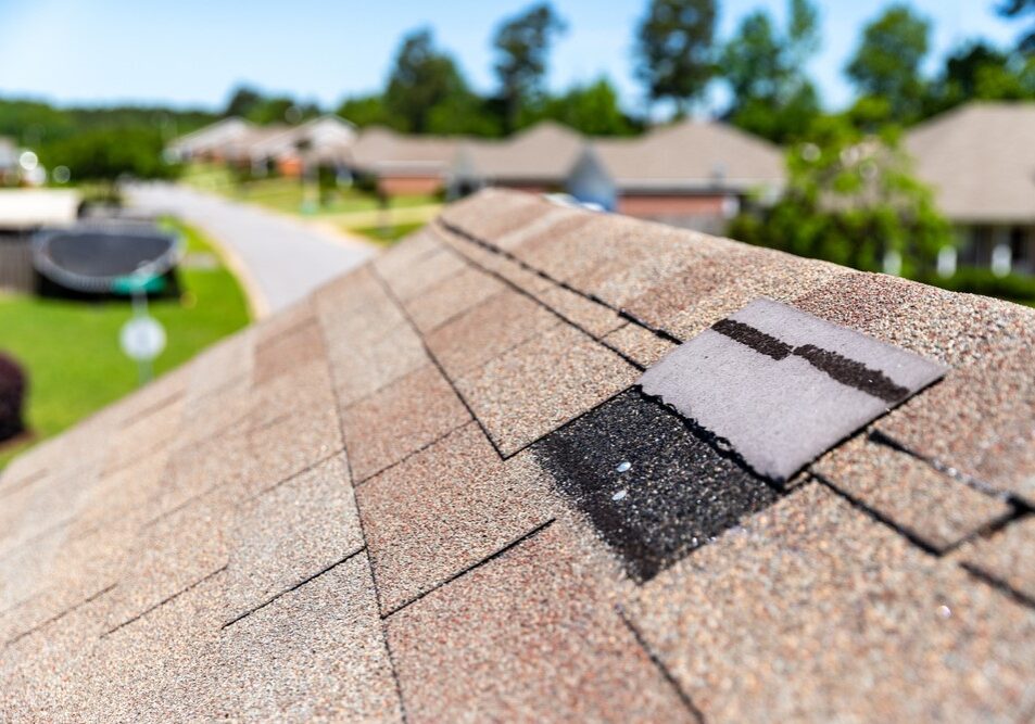 Damaged brown ridge cap shingle flipped backwards on a residential roof.