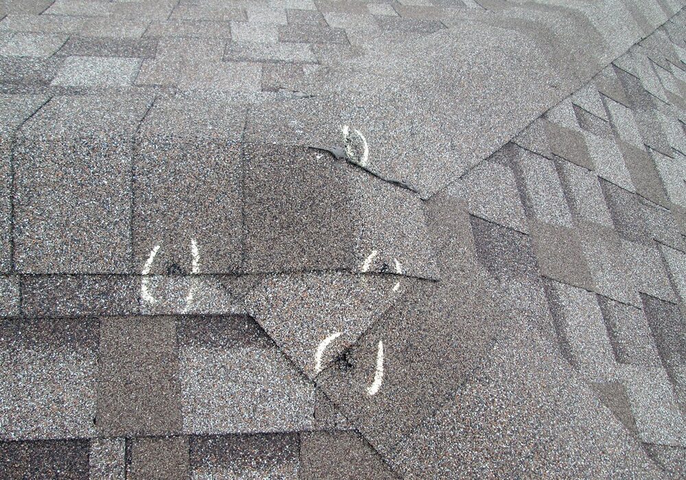 Close-up of white chalk marks highlighting damage on a shingle roof ridge cap during an inspection.