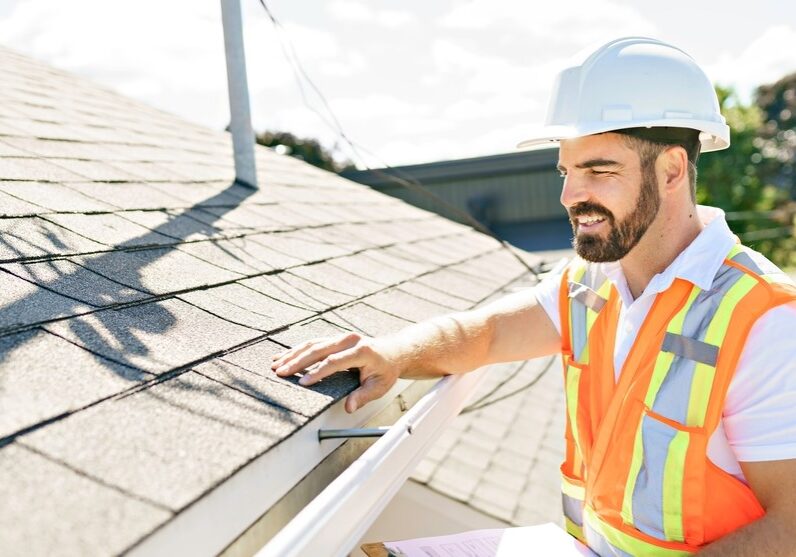 Roofing inspector checking the asphalt shingles and gutter system on a sunny day.