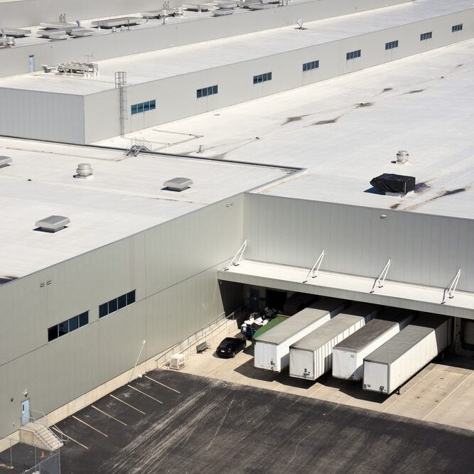 High-angle view of a large commercial warehouse flat roof and a loading dock with semi-truck trailers.
