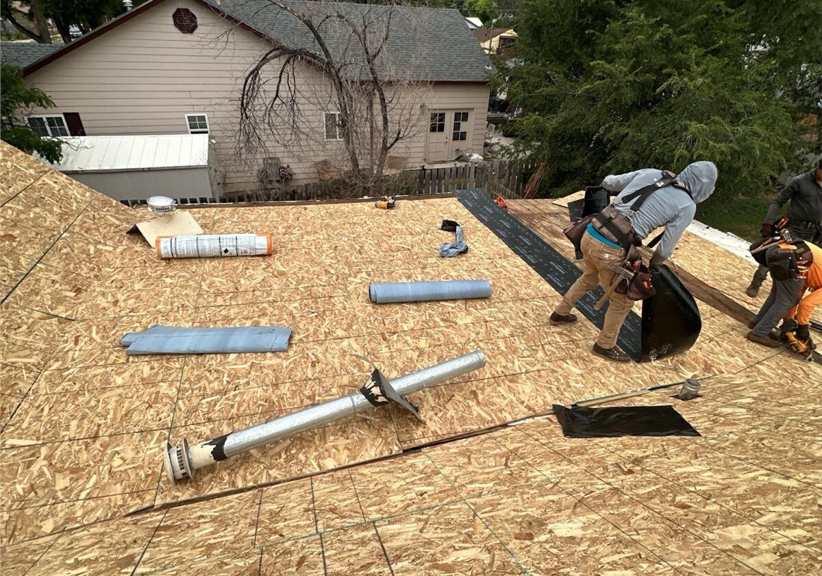 Construction workers rolling out black underlayment on a newly installed OSB plywood roof deck during a residential roof replacement.