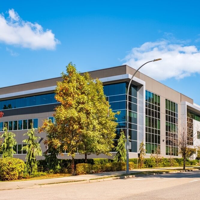 A modern, multi-story commercial office building featuring a gray facade, large glass curtain walls, and white architectural trim.